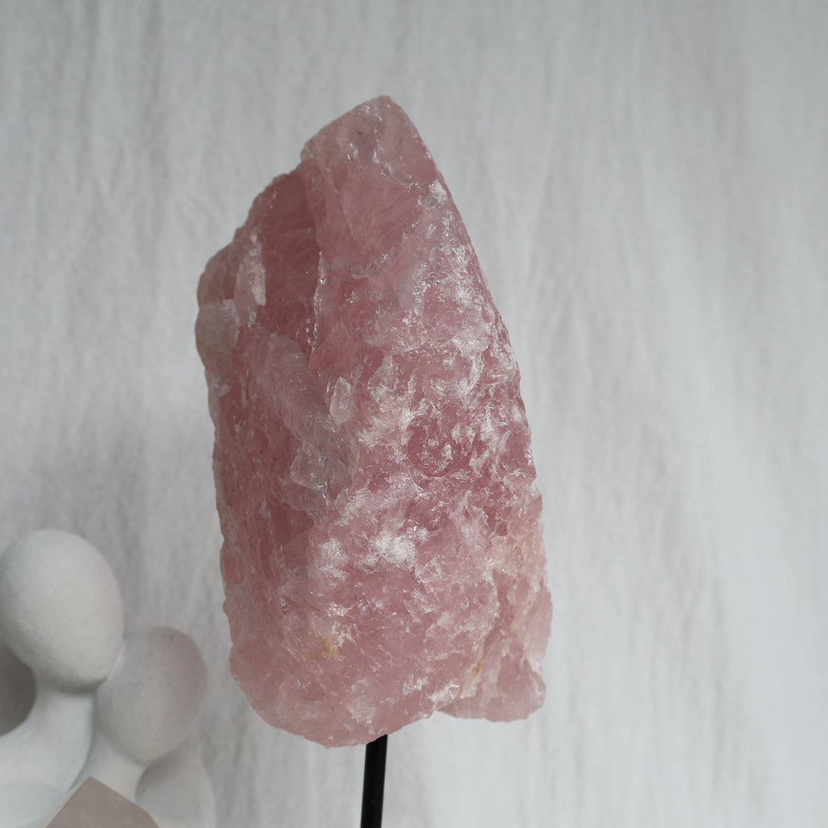 Large 1.1kg raw Rose Quartz crystal on black rotating stand with natural soft pink colouring and raw texture, standing 24cm tall.