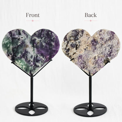 Large purple and green Fluorite heart on black stand with a roughly polished face and contrasting raw crystal reverse, 23cm tall on stand.