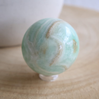 Caribbean Calcite crystal sphere, 4.4cm and 133g, with soft blue-green colouring and natural cream and sandy-toned banding.