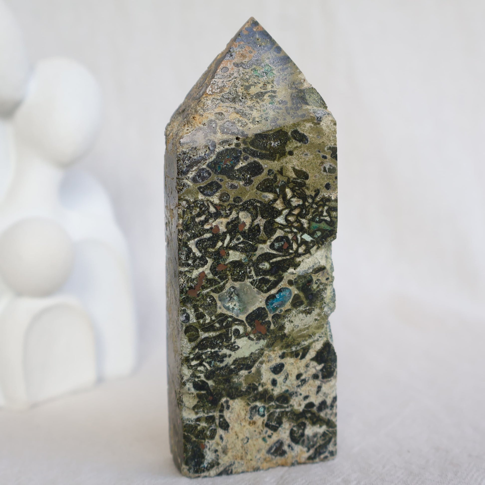 Epidote obelisk with natural Chrysocolla and copper inclusions, featuring earthy green, soft blue and metallic tones, 10.7cm tall.