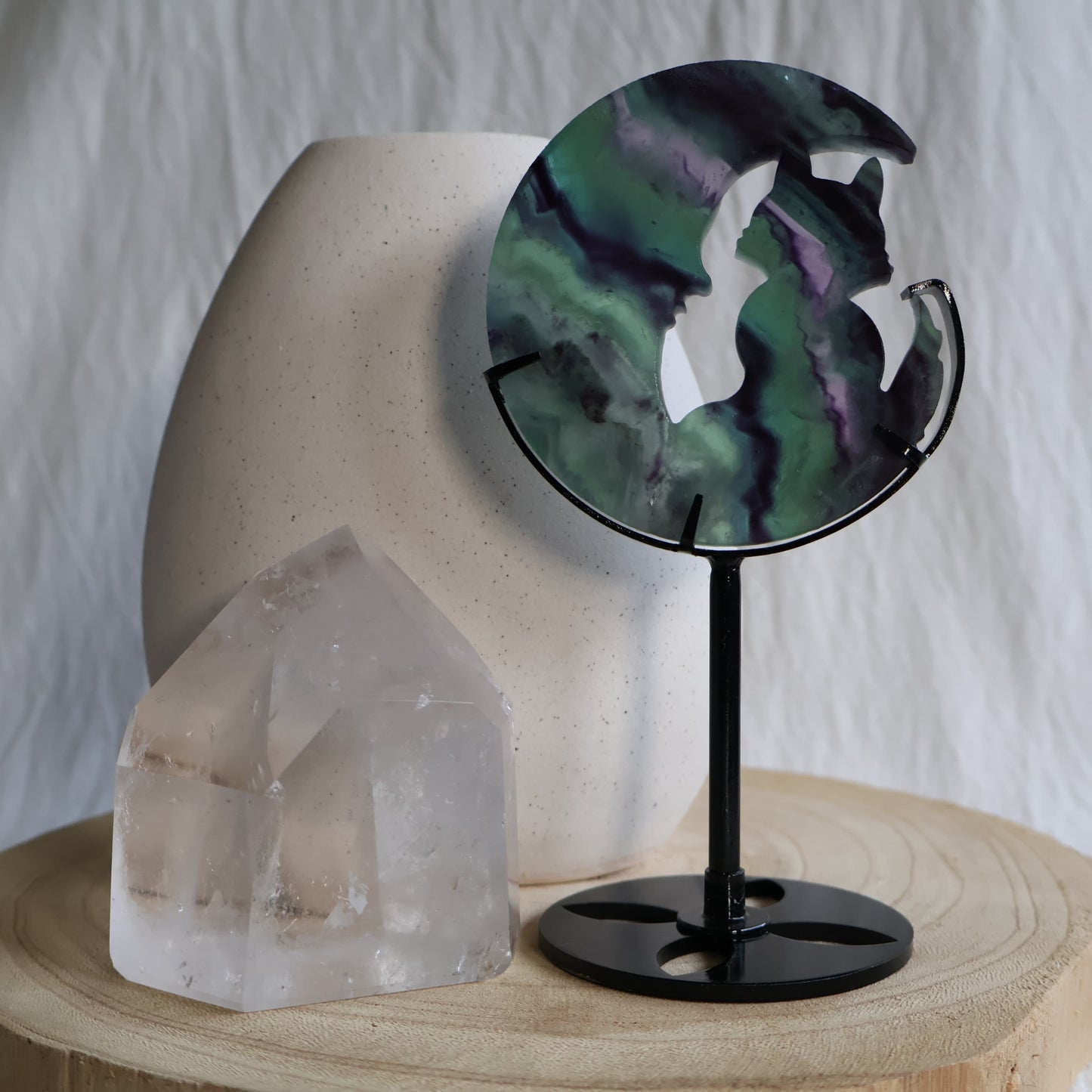 Green and purple Fluorite cat sitting within a crescent moon carving on black metal stand with natural banded colour zoning