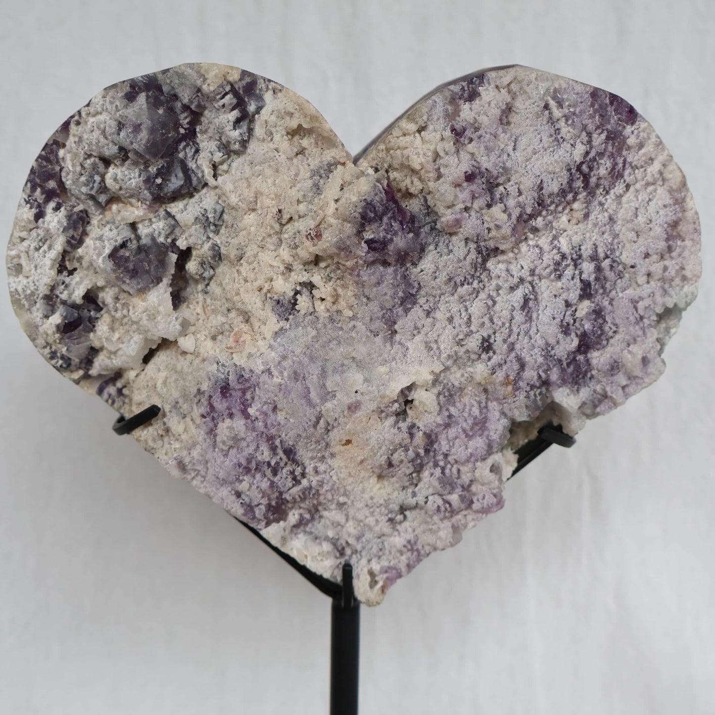 Large purple and green Fluorite heart on black stand with a roughly polished face and contrasting raw crystal reverse, 23cm tall on stand.