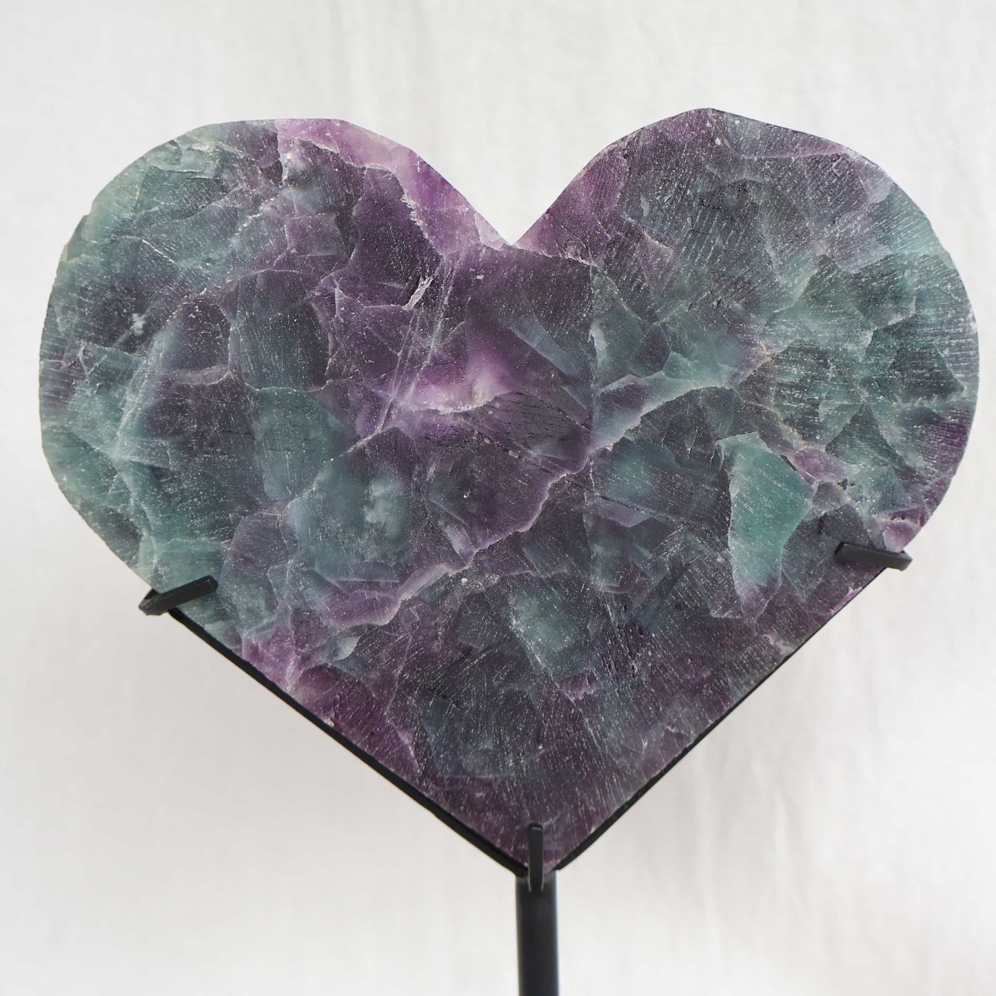 Large teal-green and purple Fluorite heart on black stand with a roughly polished face and contrasting raw lavender crystal reverse, 23cm tall.