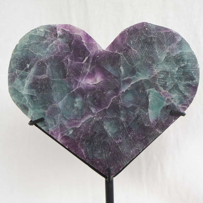 Large teal-green and purple Fluorite heart on black stand with a roughly polished face and contrasting raw lavender crystal reverse, 23cm tall.