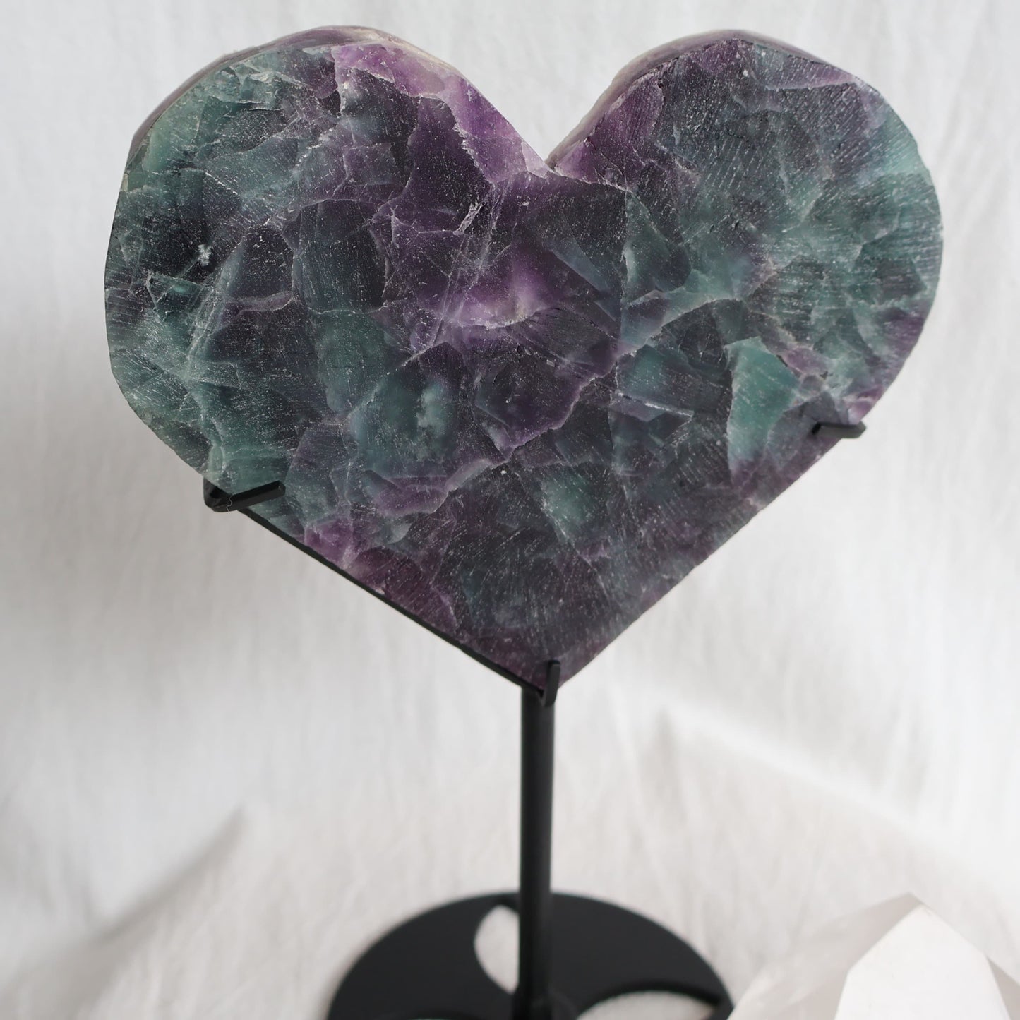 Large teal-green and purple Fluorite heart on black stand with a roughly polished face and contrasting raw lavender crystal reverse, 23cm tall.