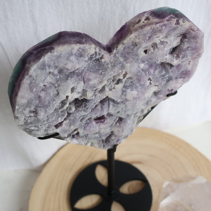 Large teal-green and purple Fluorite heart on black stand with a roughly polished face and contrasting raw lavender crystal reverse, 23cm tall.