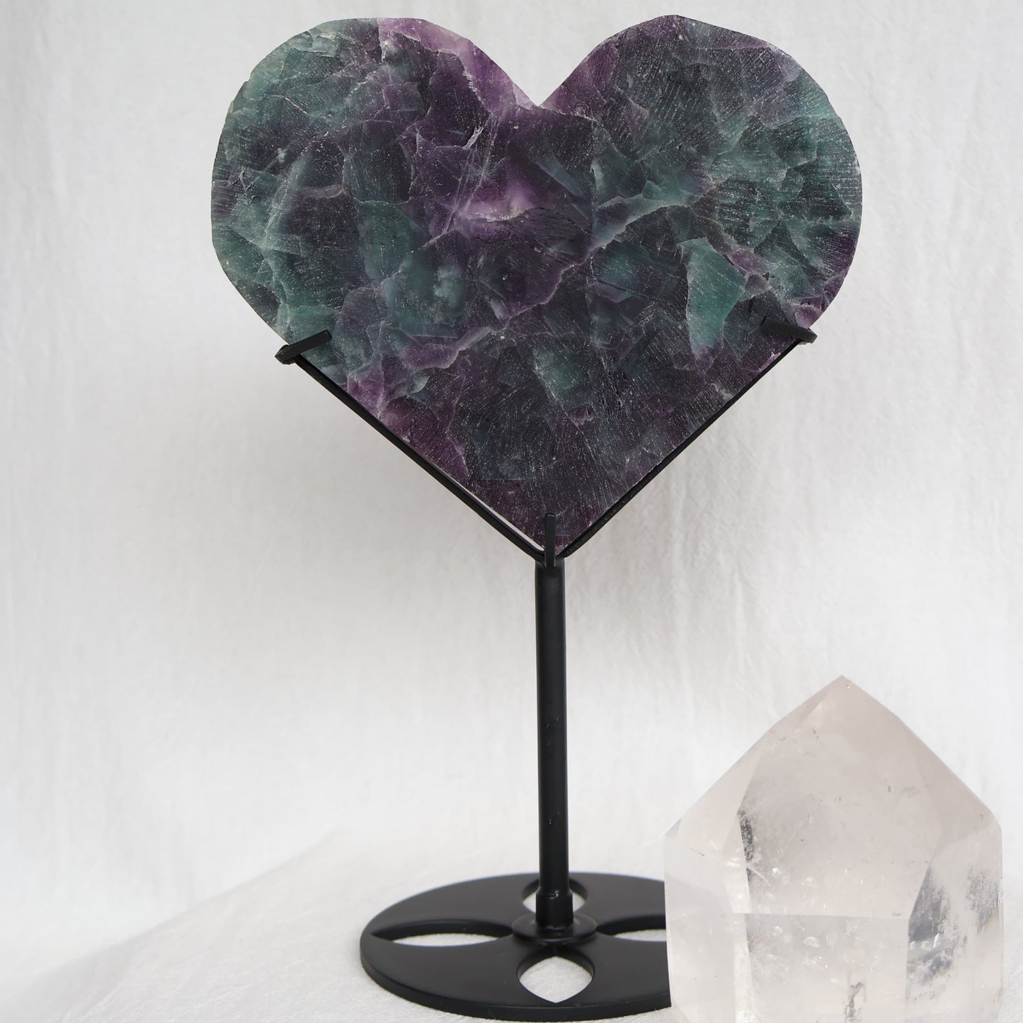 Large teal-green and purple Fluorite heart on black stand with a roughly polished face and contrasting raw lavender crystal reverse, 23cm tall.