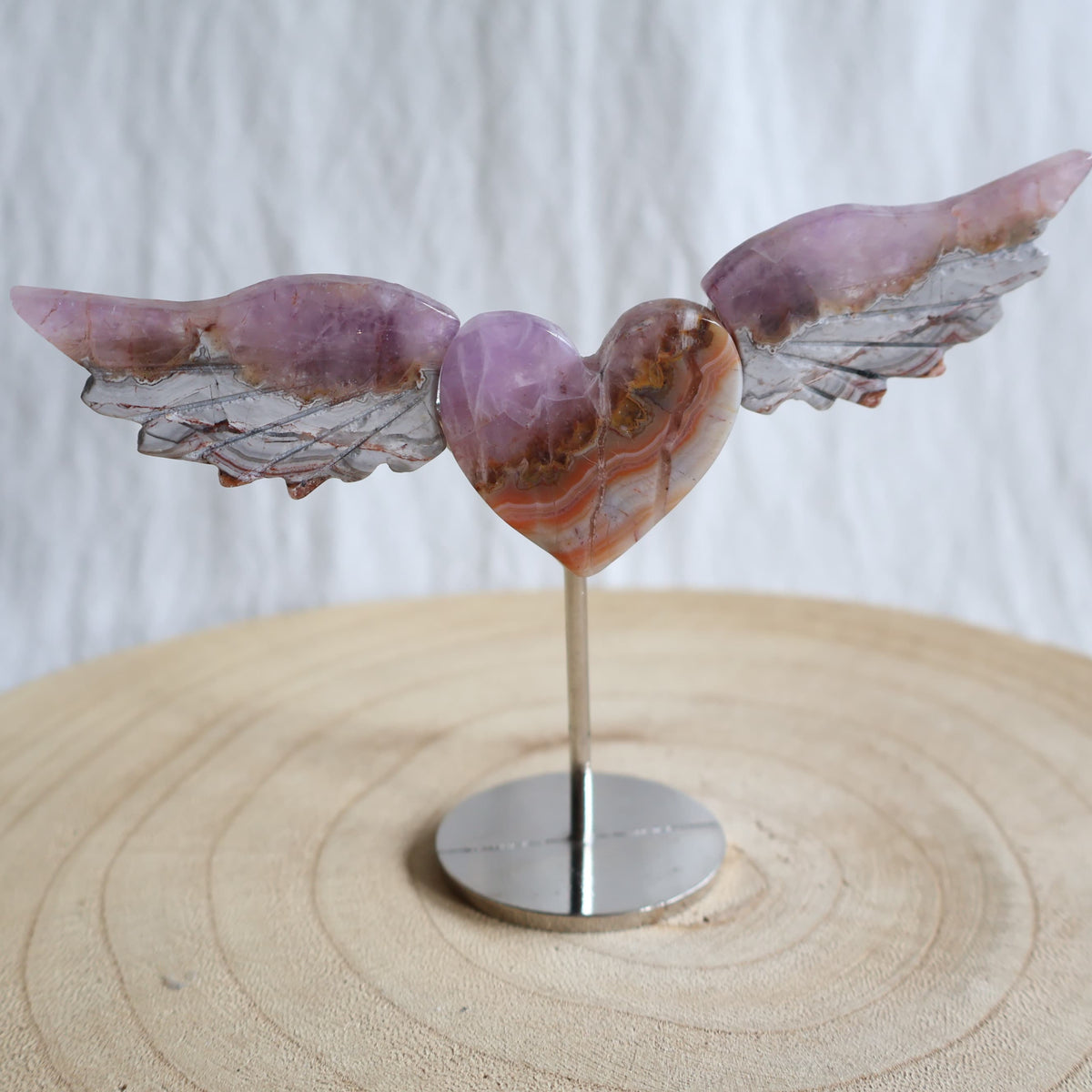 Crystal heart with carved wings in natural Moss Agate, Sodalite, Fire Quartz or Amethyst Agate, displayed upright on a silver-toned stand.
