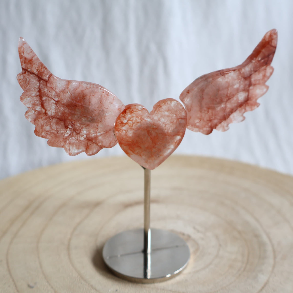 Crystal heart with carved wings in natural Moss Agate, Sodalite, Fire Quartz or Amethyst Agate, displayed upright on a silver-toned stand.