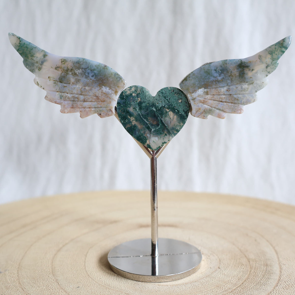 Crystal heart with carved wings in natural Moss Agate, Sodalite, Fire Quartz or Amethyst Agate, displayed upright on a silver-toned stand.