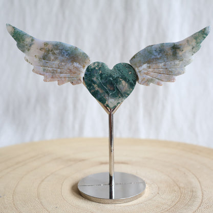 Crystal heart with carved wings in natural Moss Agate, Sodalite, Fire Quartz or Amethyst Agate, displayed upright on a silver-toned stand.