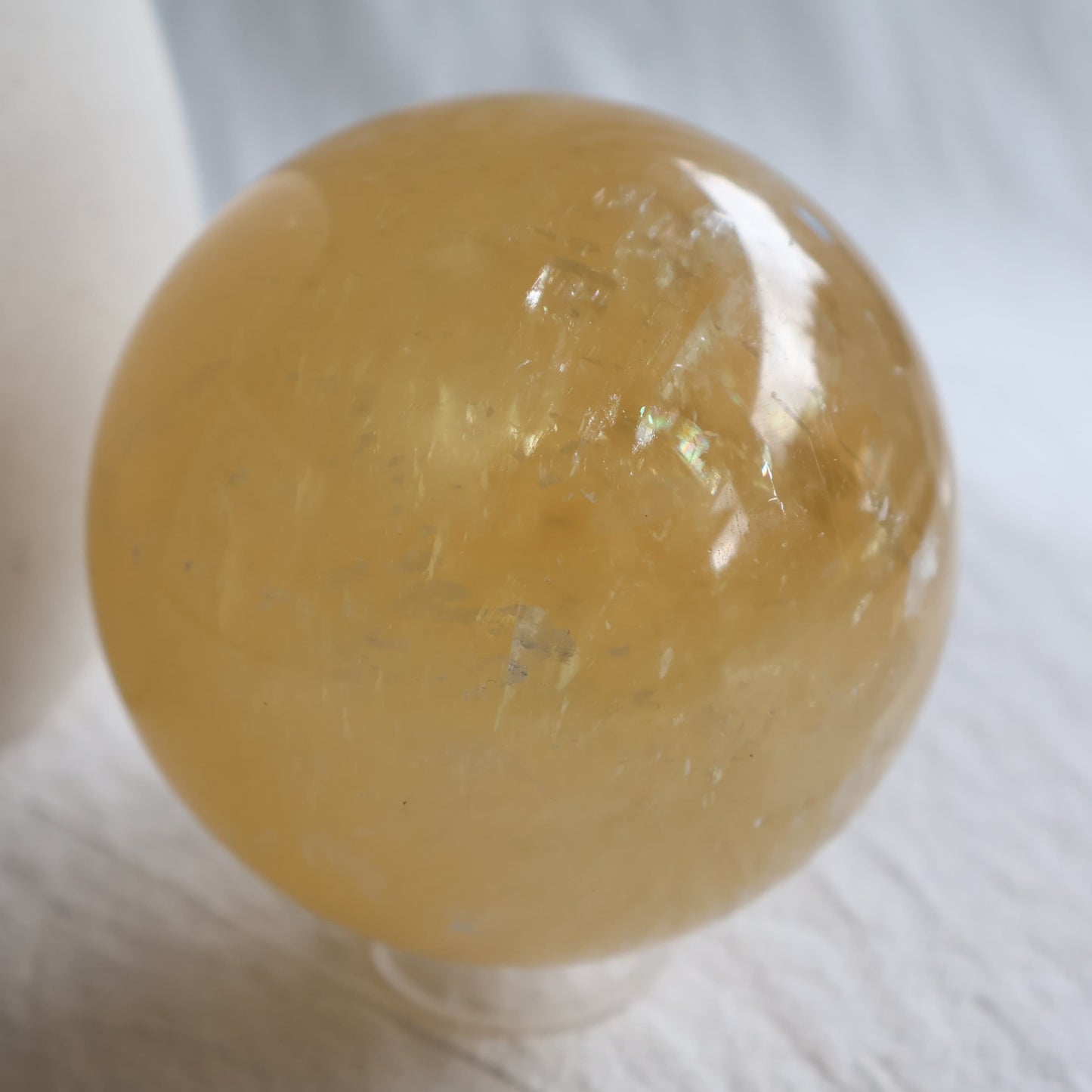 Large Honey Calcite crystal sphere with translucent golden yellow colouring, natural internal formations and rainbow flashes.