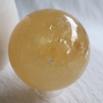 Large Honey Calcite crystal sphere with translucent golden yellow colouring, natural internal formations and rainbow flashes.