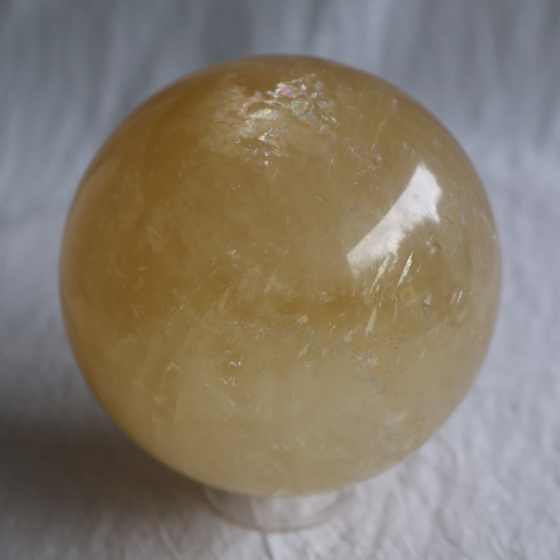Large Honey Calcite crystal sphere with translucent golden yellow colouring, natural internal formations and rainbow flashes.