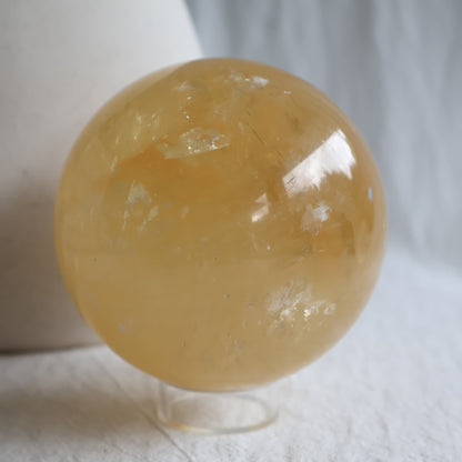 Large Honey Calcite crystal sphere with translucent golden yellow colouring, natural internal formations and rainbow flashes.