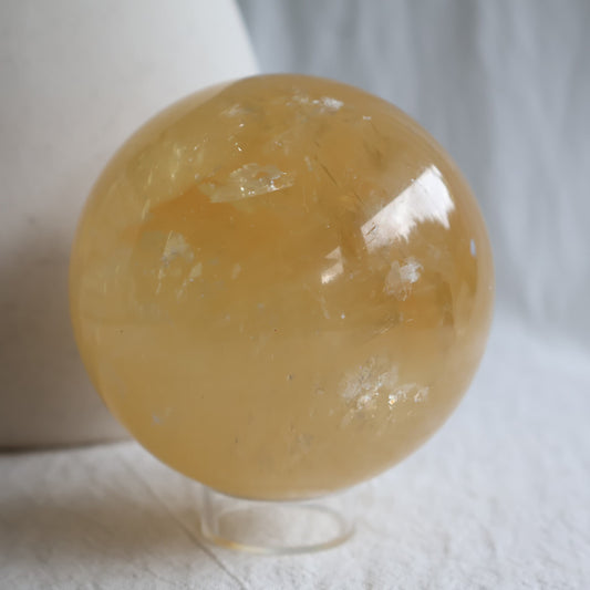Large Honey Calcite crystal sphere with translucent golden yellow colouring, natural internal formations and rainbow flashes.