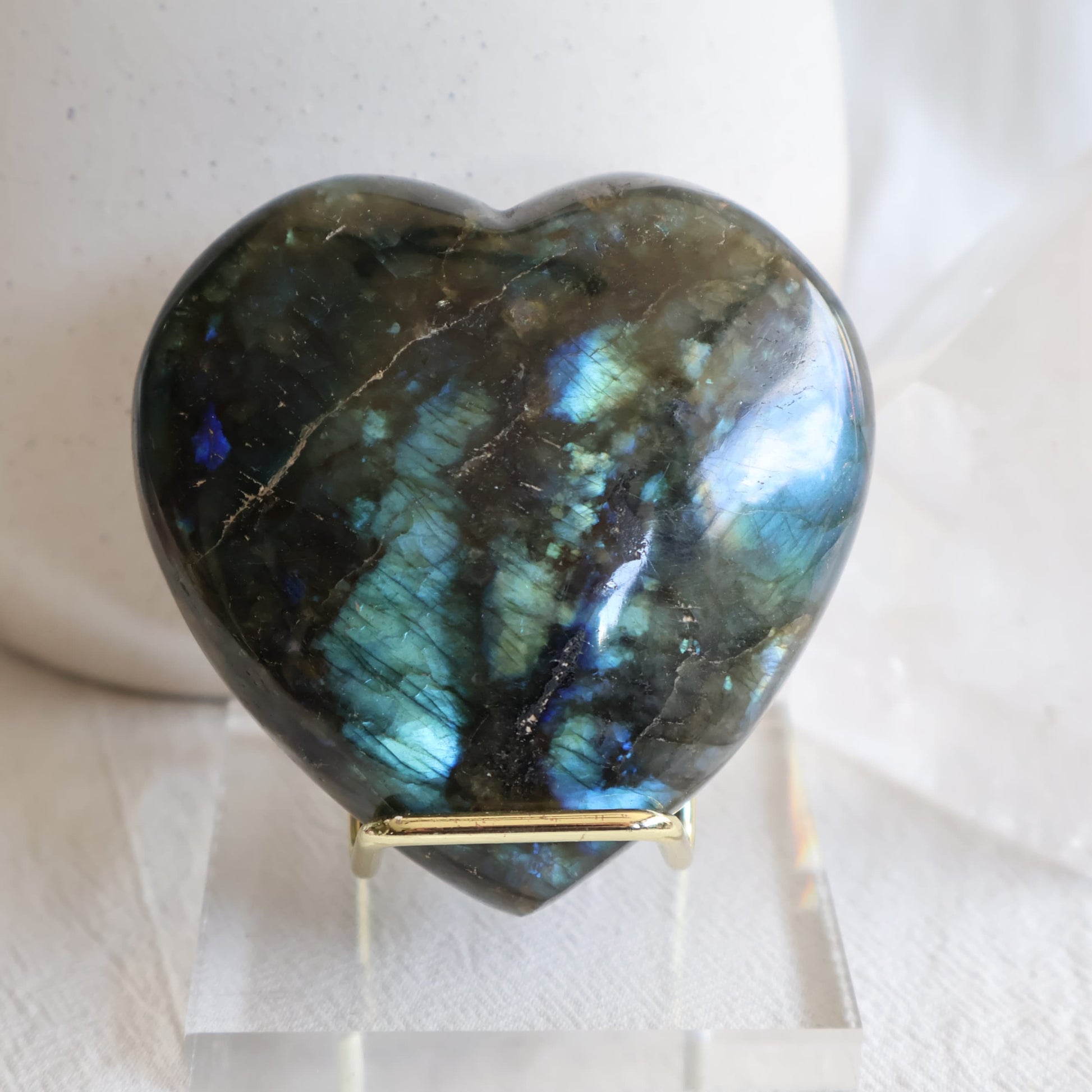 Labradorite crystal heart with bright blue and teal flash on a gold-toned display stand.