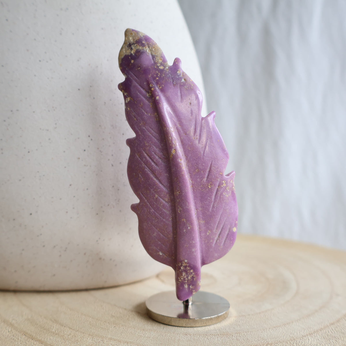 Purple Phosphosiderite crystal feather carving with natural earthy inclusions displayed upright on a silver-toned stand.