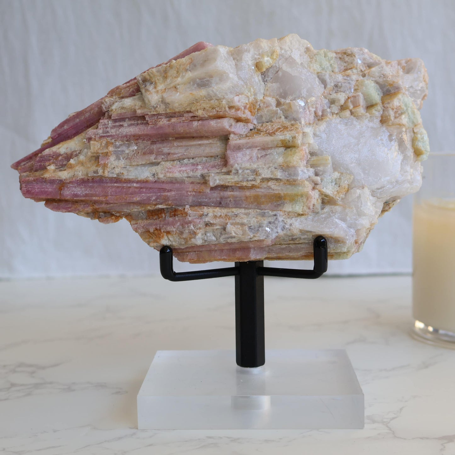 Large pink tourmaline in quartz matrix specimen with elongated pink tourmaline crystals running through white quartz and feldspar matrix displayed on a stand.