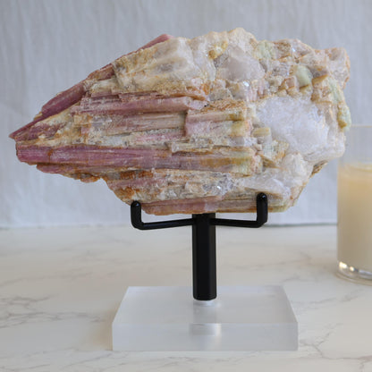 Large pink tourmaline in quartz matrix specimen with elongated pink tourmaline crystals running through white quartz and feldspar matrix displayed on a stand.
