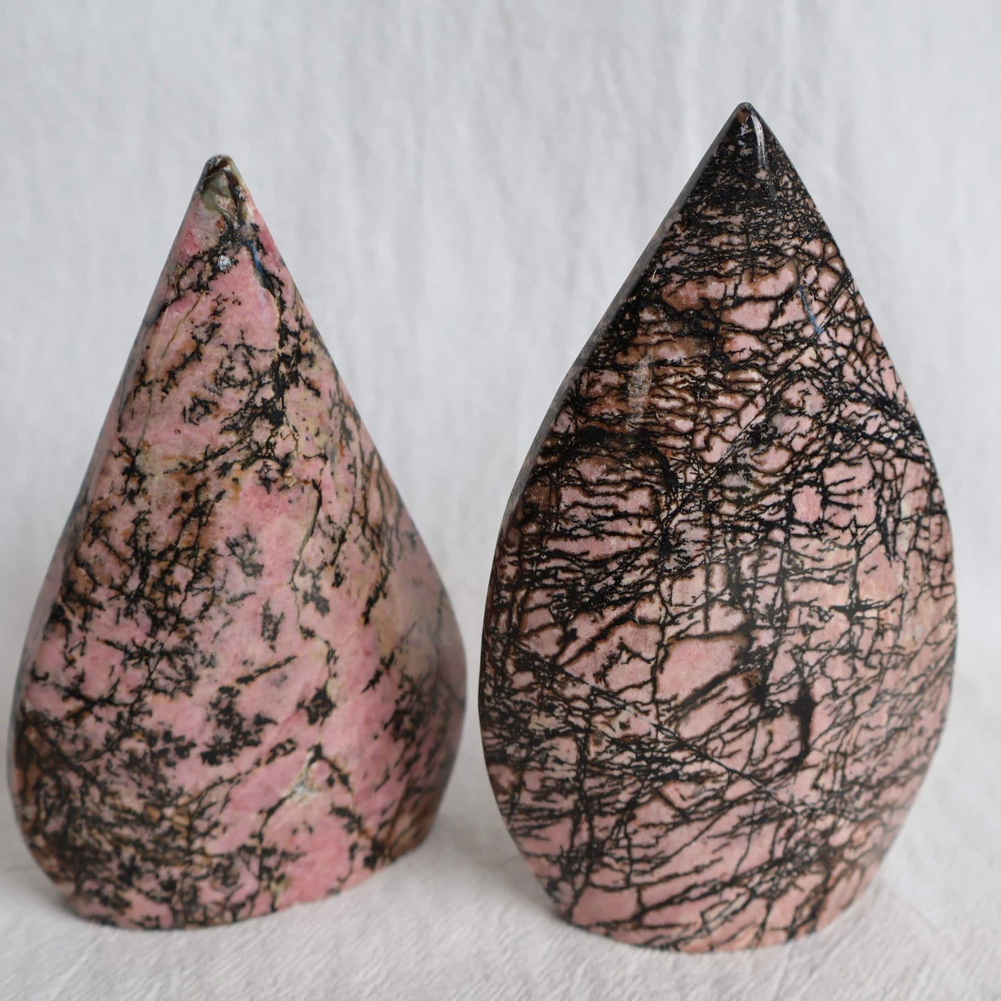 Pink Rhodonite teardrop carving with natural black veining and markings, polished into a smooth freestanding display piece.
