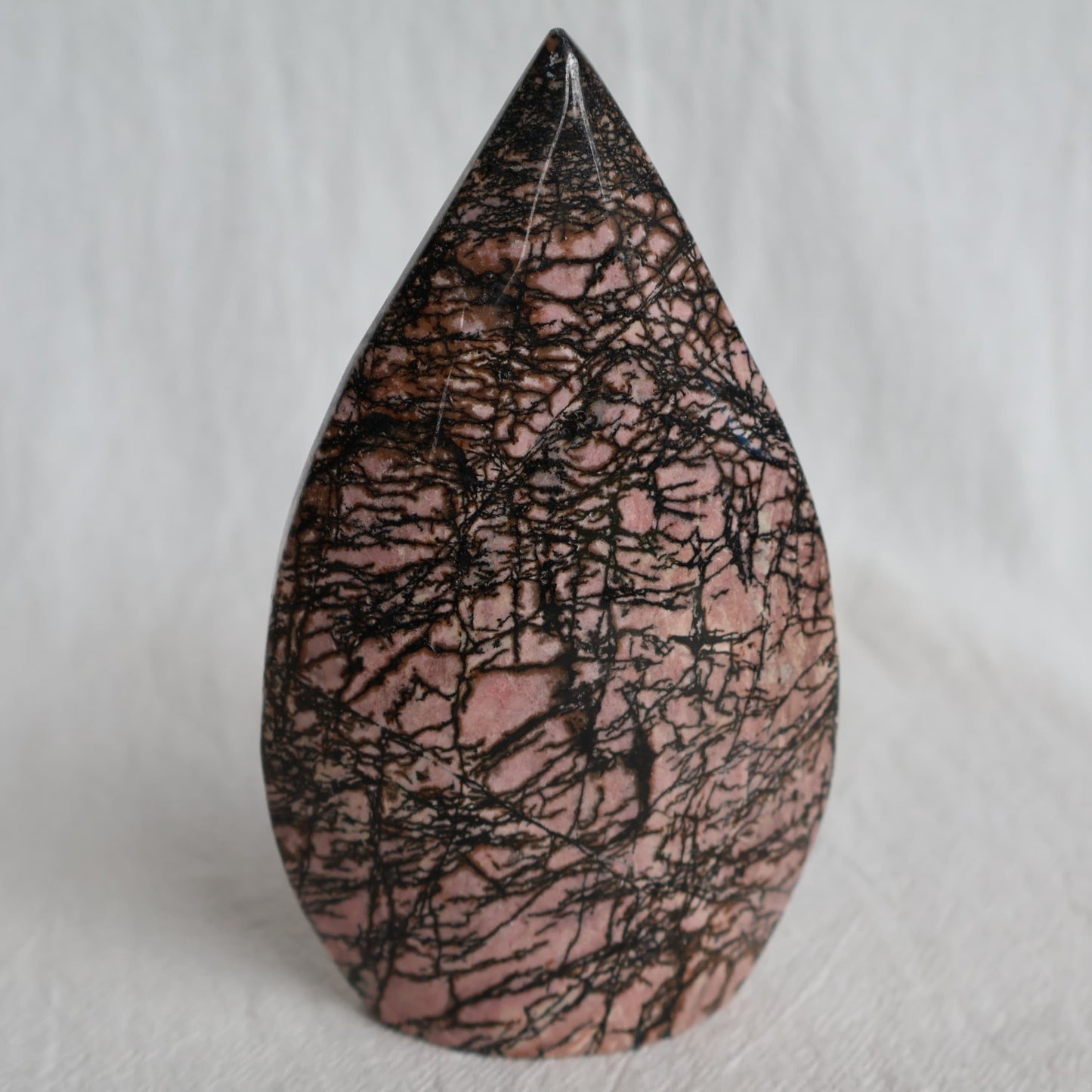 Pink Rhodonite teardrop carving with natural black veining and markings, polished into a smooth freestanding display piece.