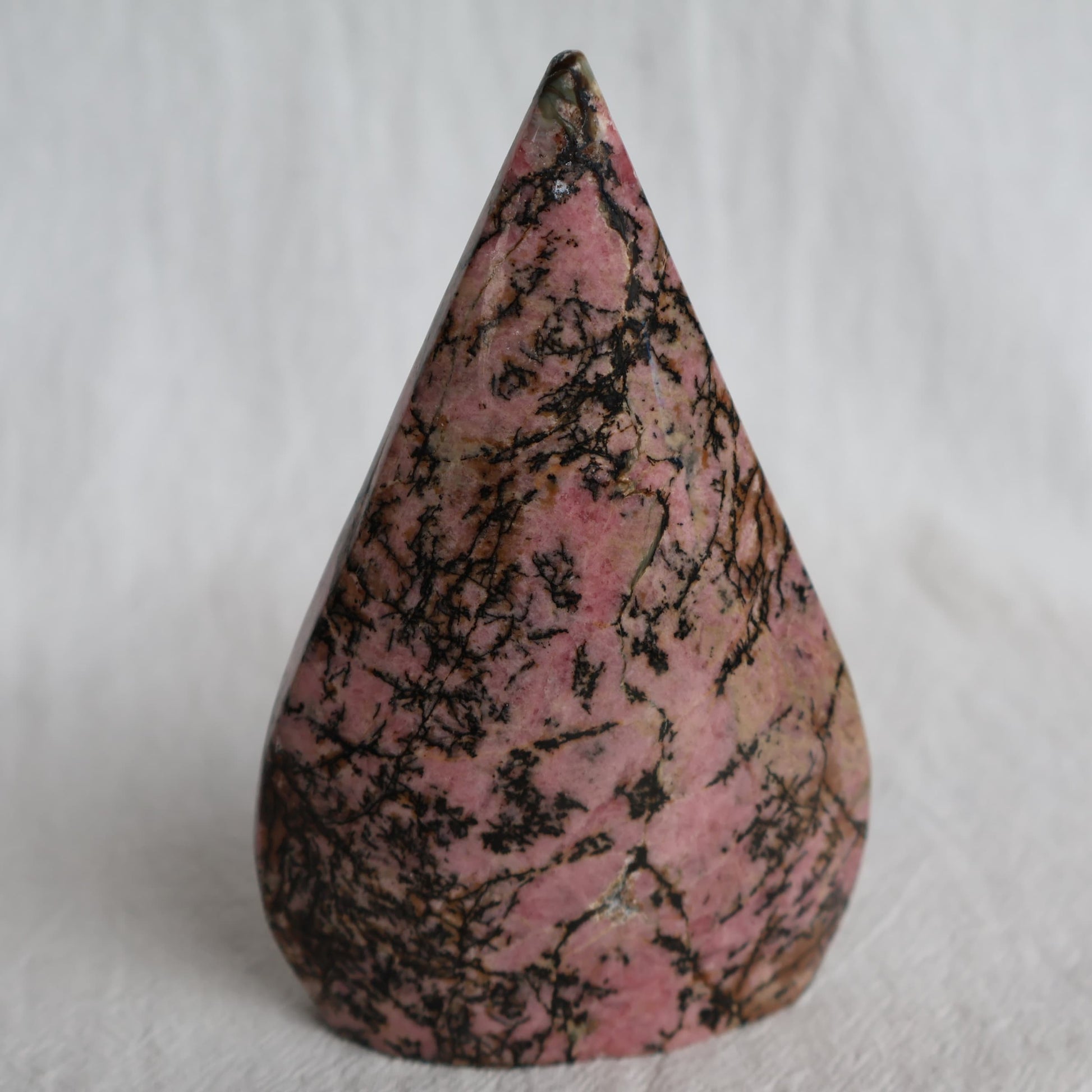Pink Rhodonite teardrop carving with natural black veining and markings, polished into a smooth freestanding display piece.