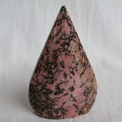Pink Rhodonite teardrop carving with natural black veining and markings, polished into a smooth freestanding display piece.