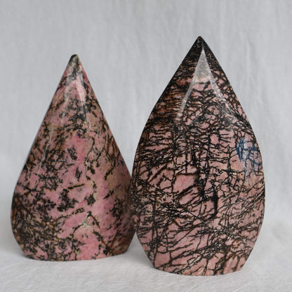 Pink Rhodonite teardrop carving with natural black veining and markings, polished into a smooth freestanding display piece.