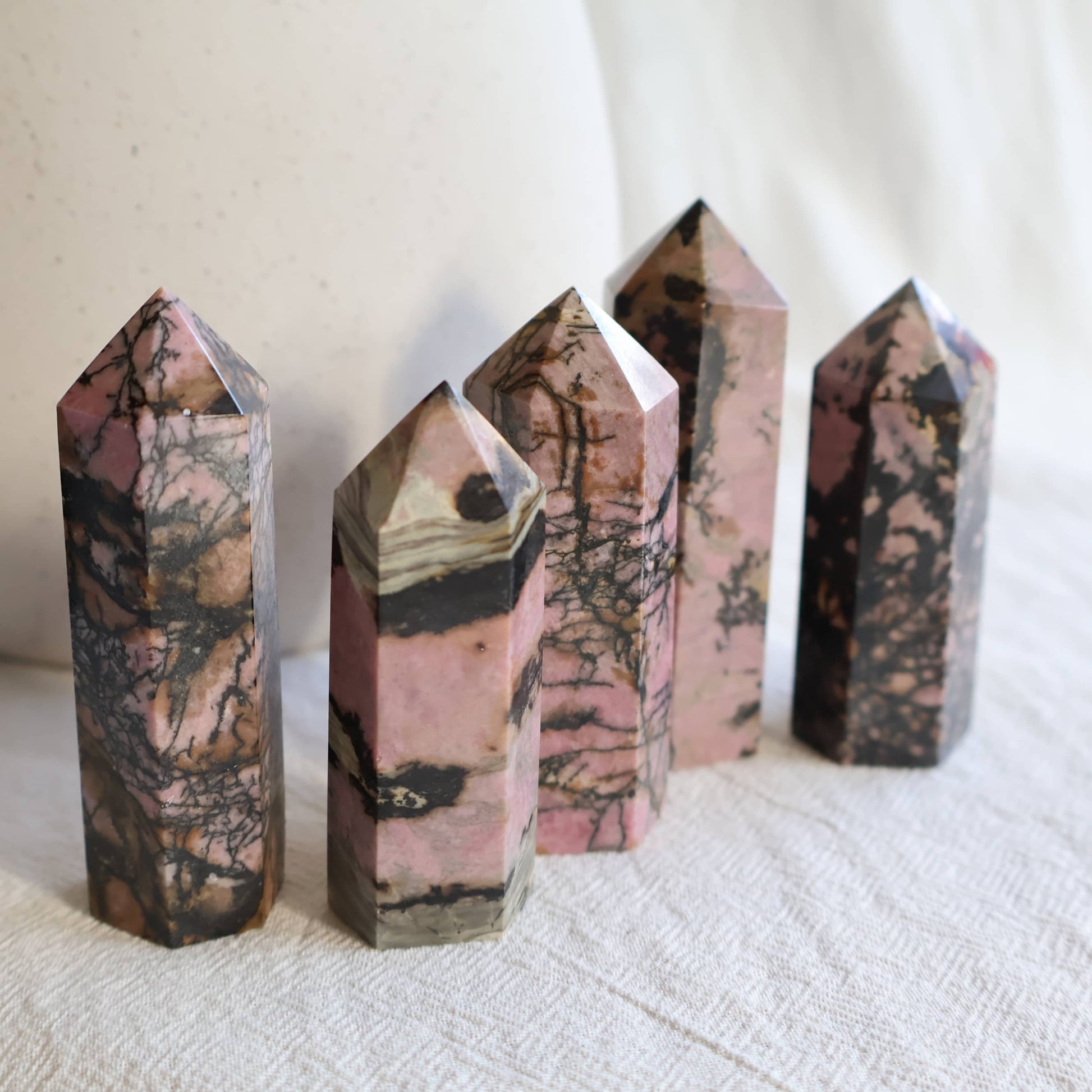 Pink Rhodonite crystal generator with natural black manganese veining and earthy patterning, polished into a pointed tower.