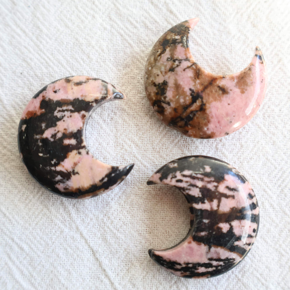 Small 3cm Rhodonite crystal moon carving with natural pink and dark manganese markings.