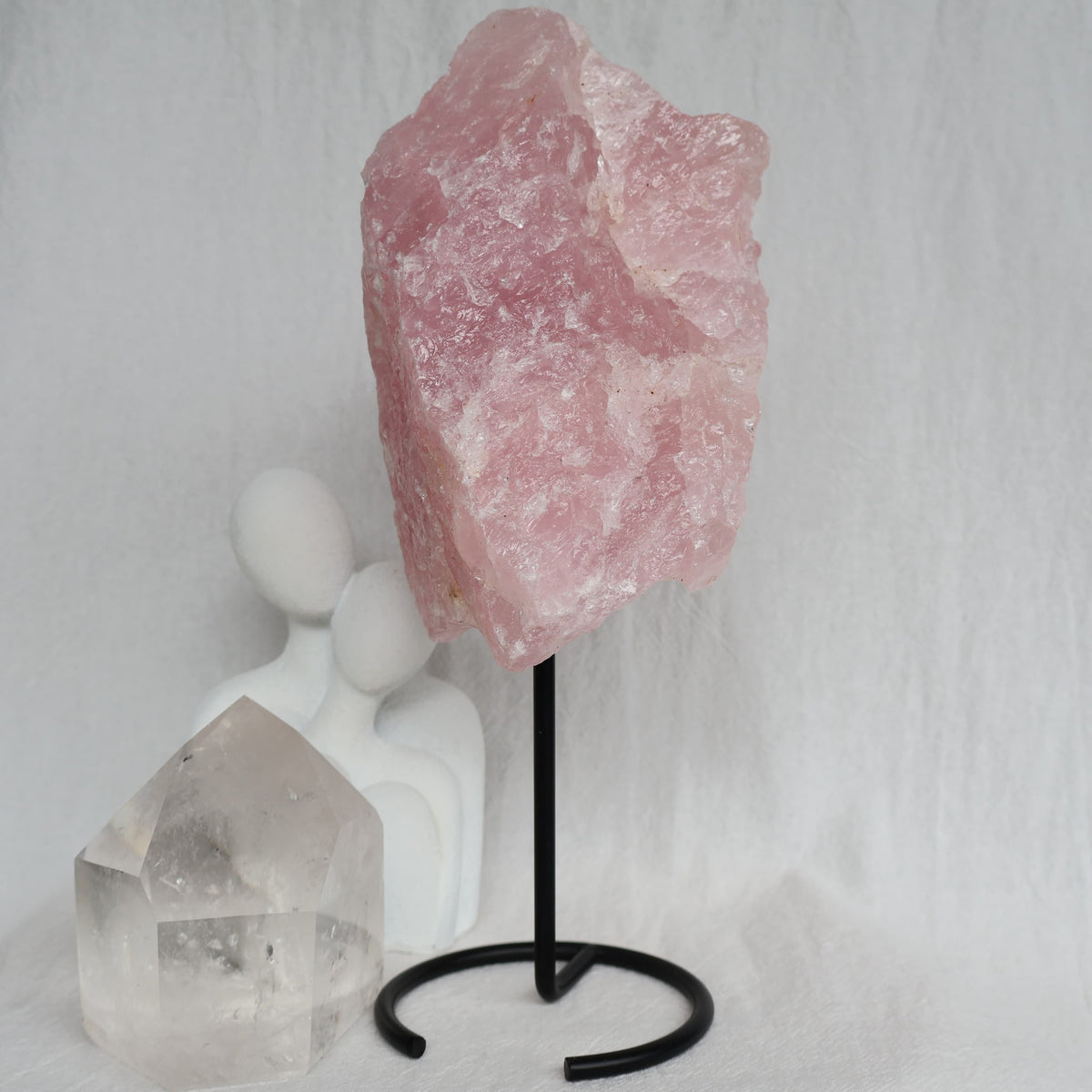 Large 1.1kg raw Rose Quartz crystal on black rotating stand with natural soft pink colouring and raw texture, standing 24cm tall.