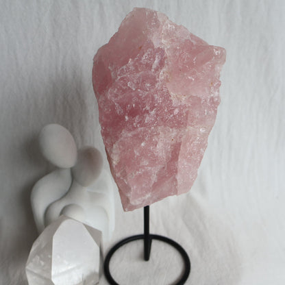Large 1.1kg raw Rose Quartz crystal on black rotating stand with natural soft pink colouring and raw texture, standing 24cm tall.