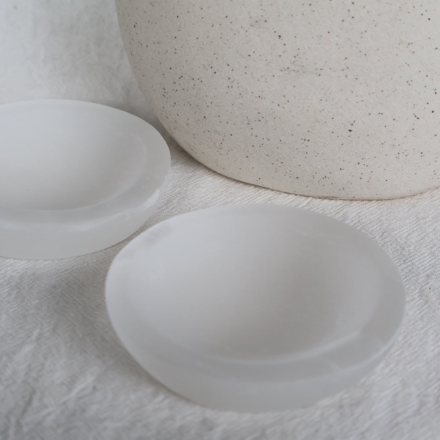 Small round Satin Spar crystal bowl approximately 7cm wide with luminous white colouring and a natural silky, pearly sheen.