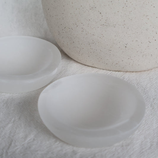 Small round Satin Spar crystal bowl approximately 7cm wide with luminous white colouring and a natural silky, pearly sheen.