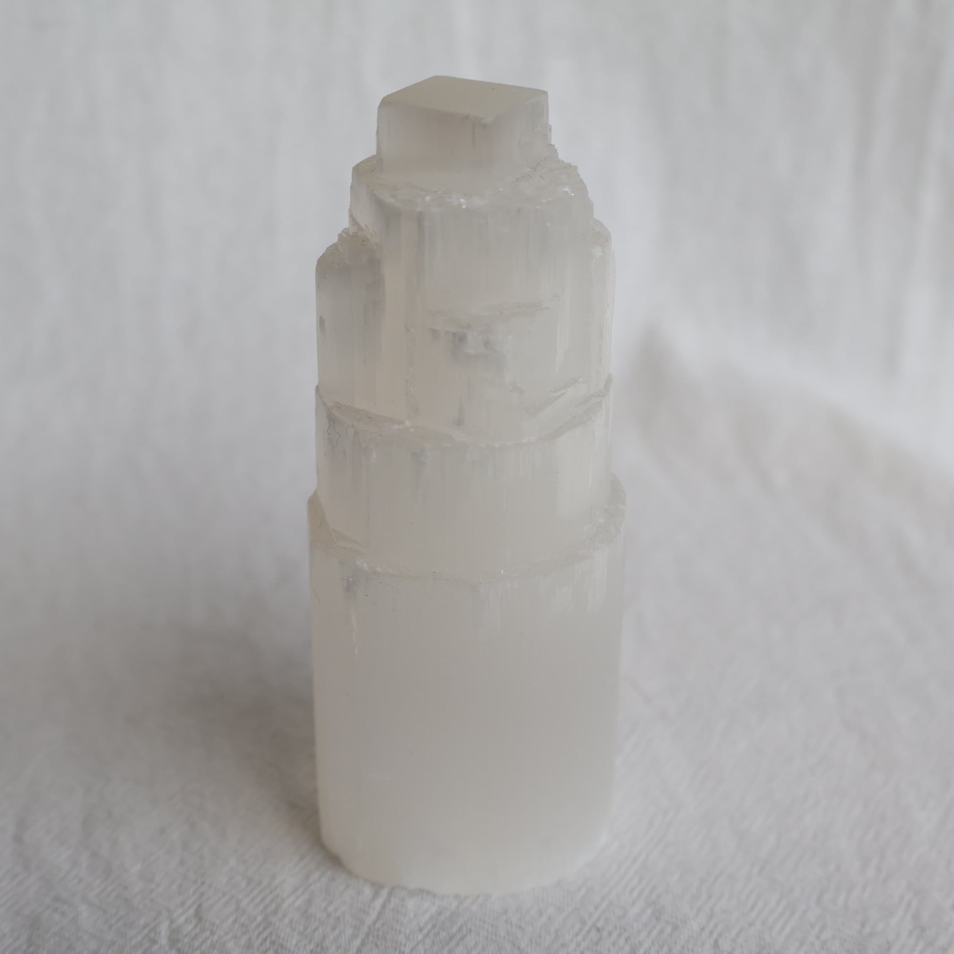 Satin Spar carved crystal tower approximately 10cm tall with luminous white colouring and natural silky fibrous striations.