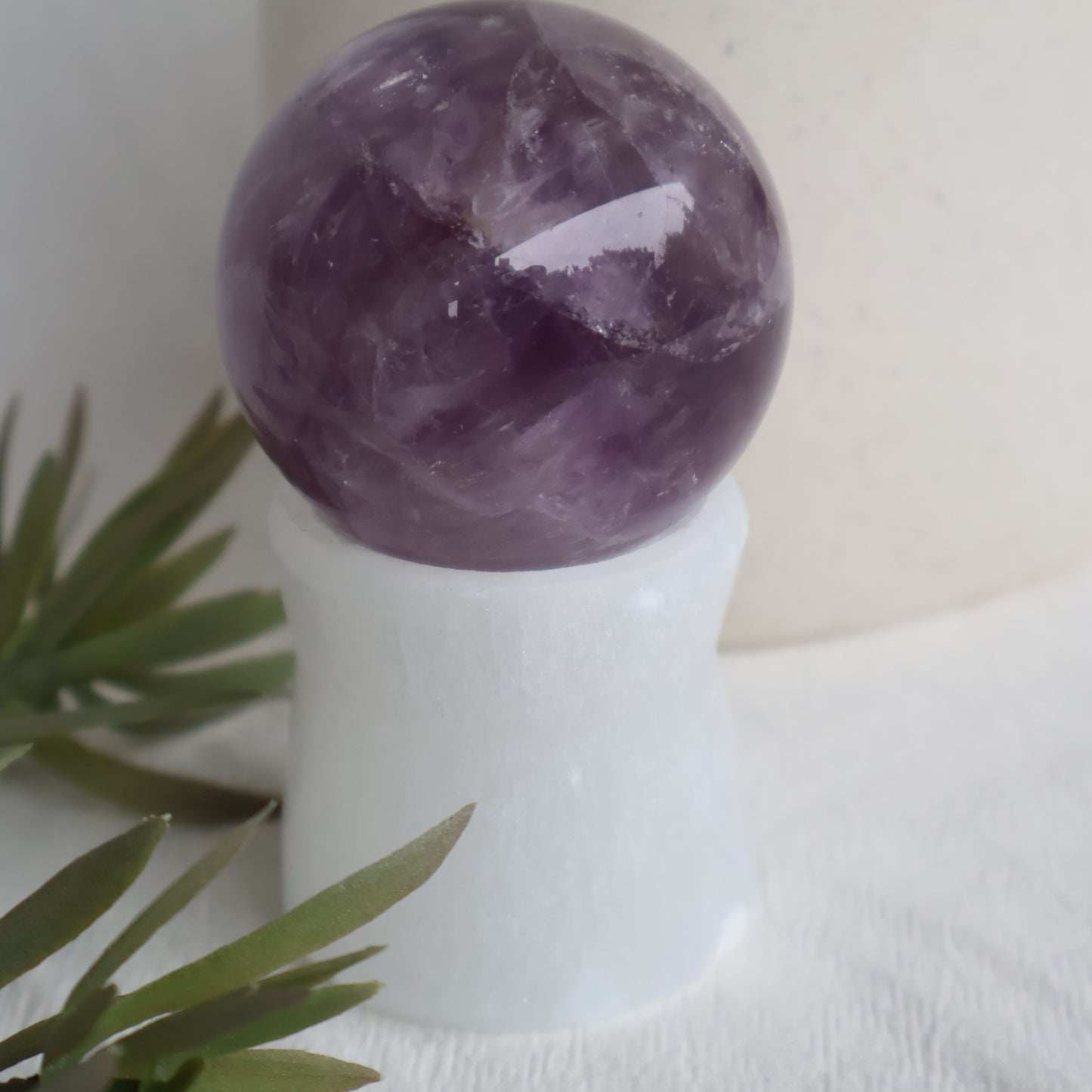 Purple crystal ball on a white stand with green leaves in the foreground