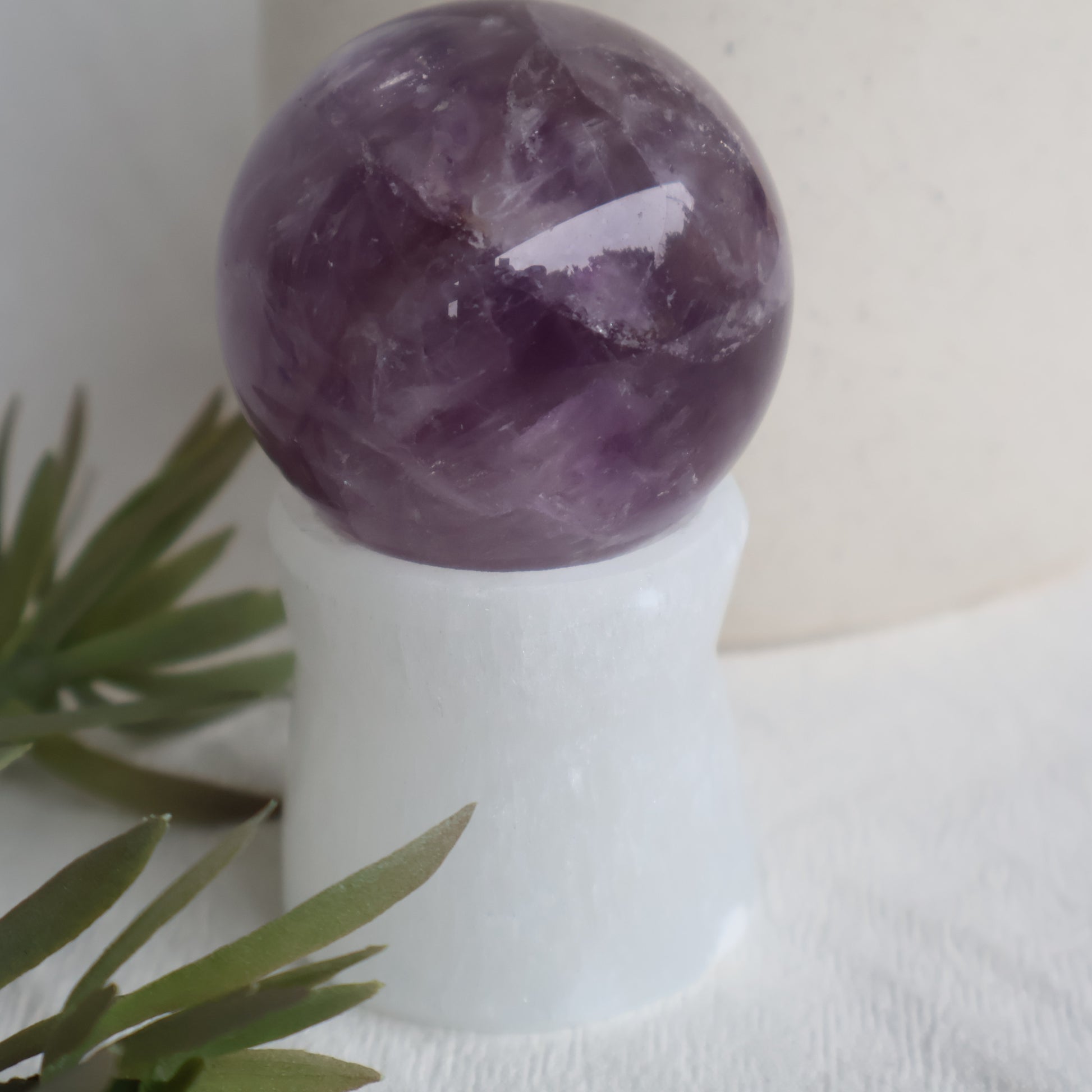 Purple crystal ball on a white stand with green leaves in the foreground