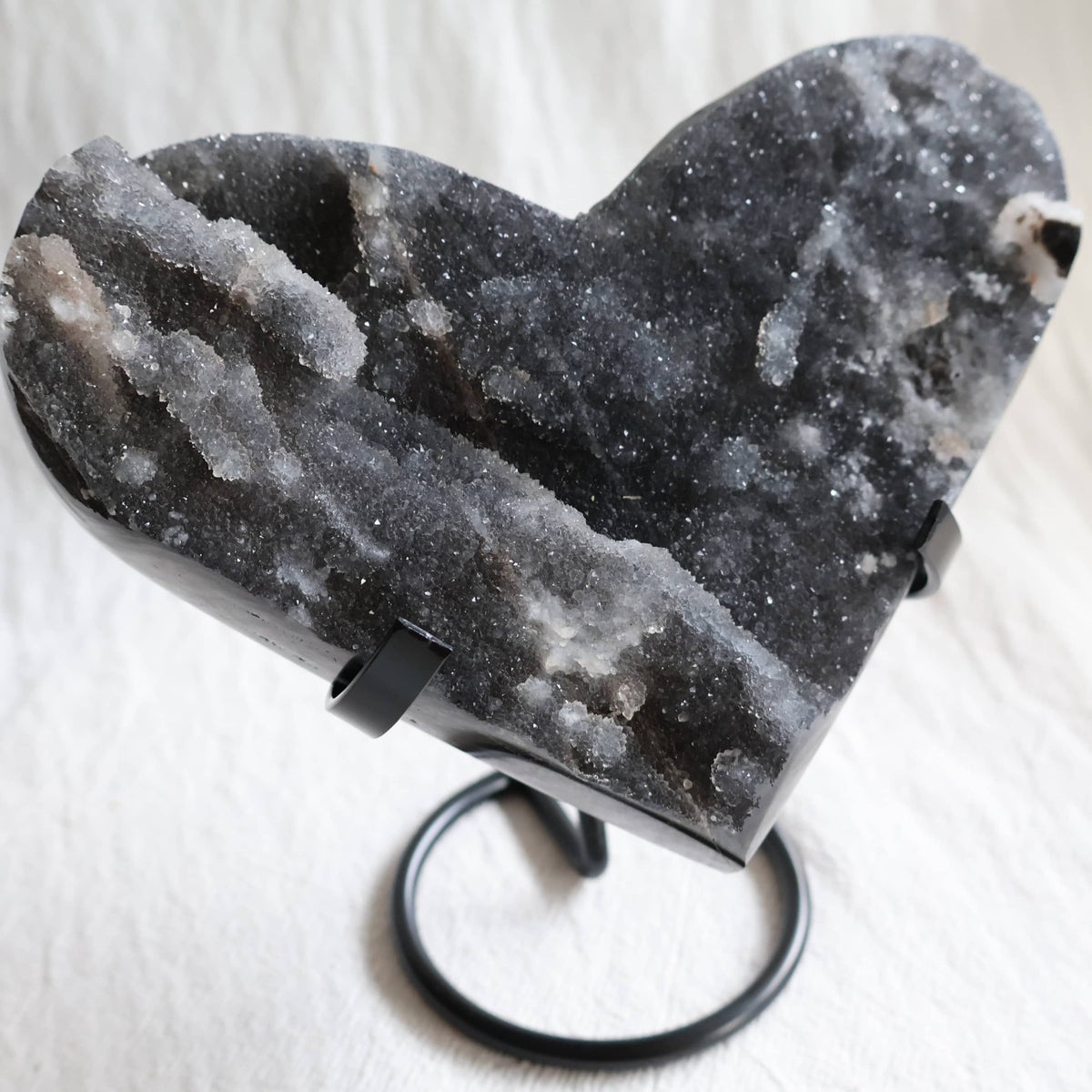 Large Sphalerite druzy crystal heart with dark charcoal-grey sparkling crystal formations displayed on a black metal stand.